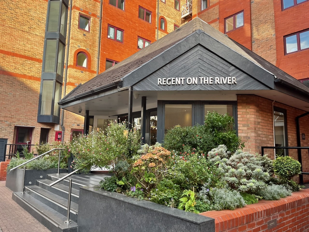 The Regent on the River entrance pavilion, with a slate roof and a raised flower bed in front